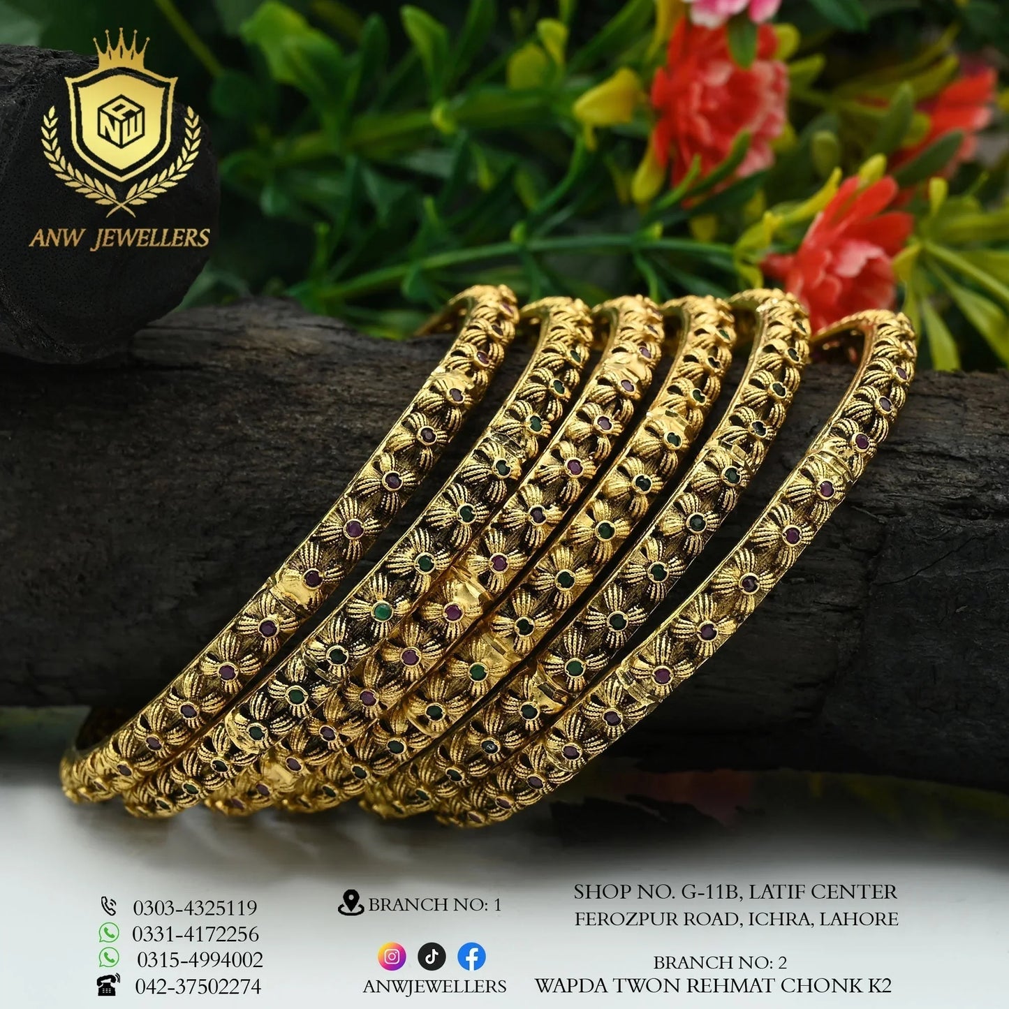 Intricately designed gold bangles by ANW Jewellers displayed on wood with floral background.