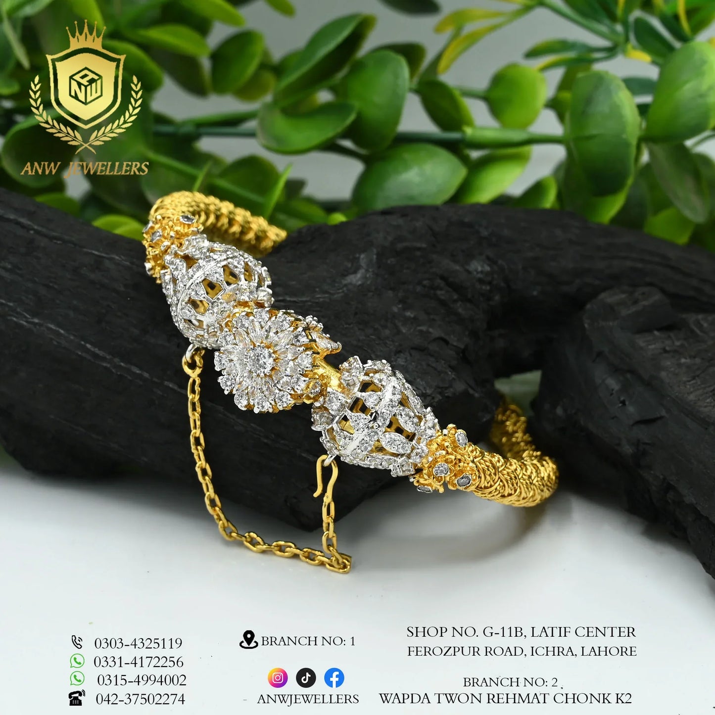 Gold and diamond-studded designer bangle by ANW Jewellers with floral detailing, displayed on black stone with green leaves.