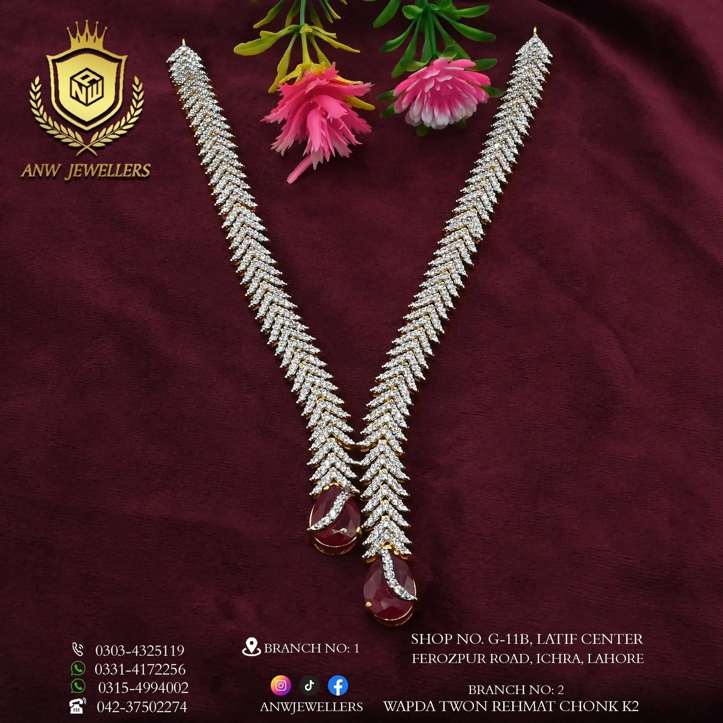 Gold and diamond necklace set with red gemstone drops on maroon fabric, ANW Jewellers branding visible