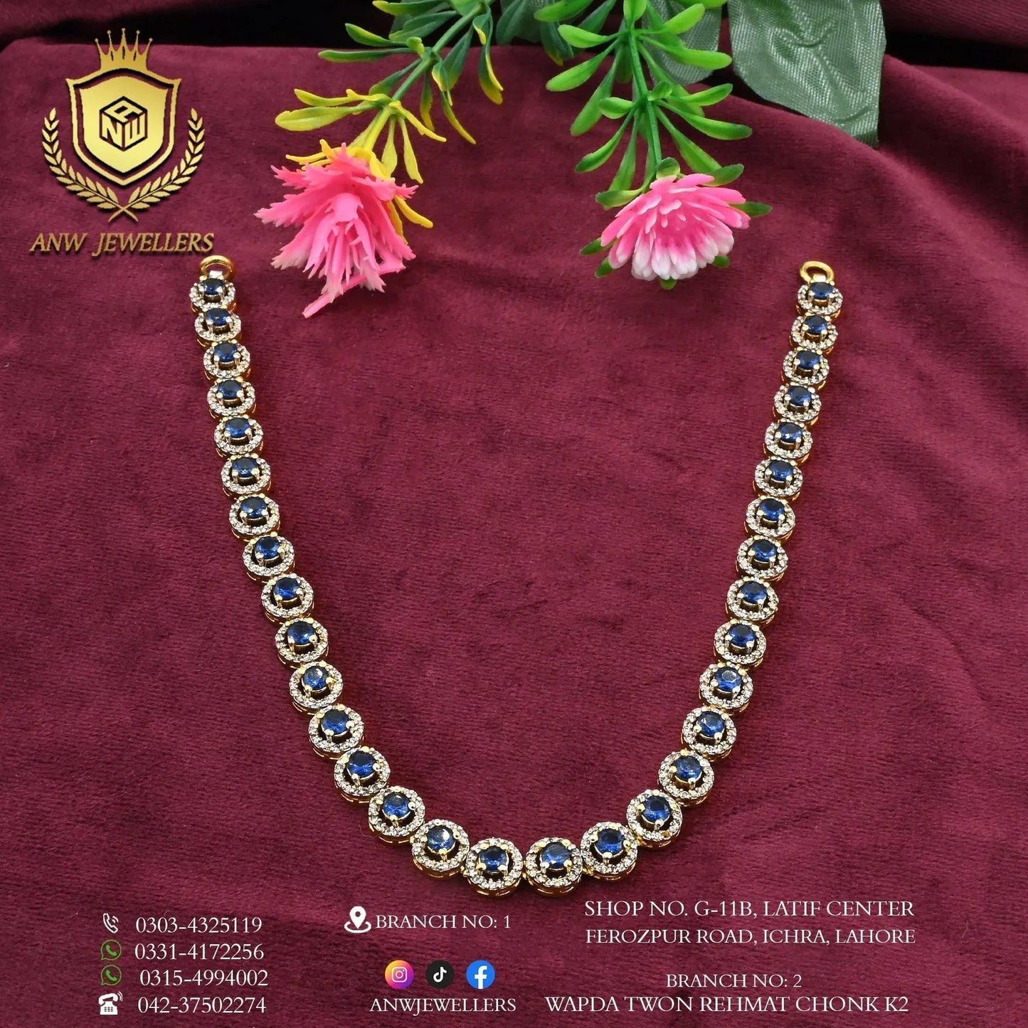 Gold and blue gemstone necklace by ANW Jewellers on maroon fabric with artificial flowers