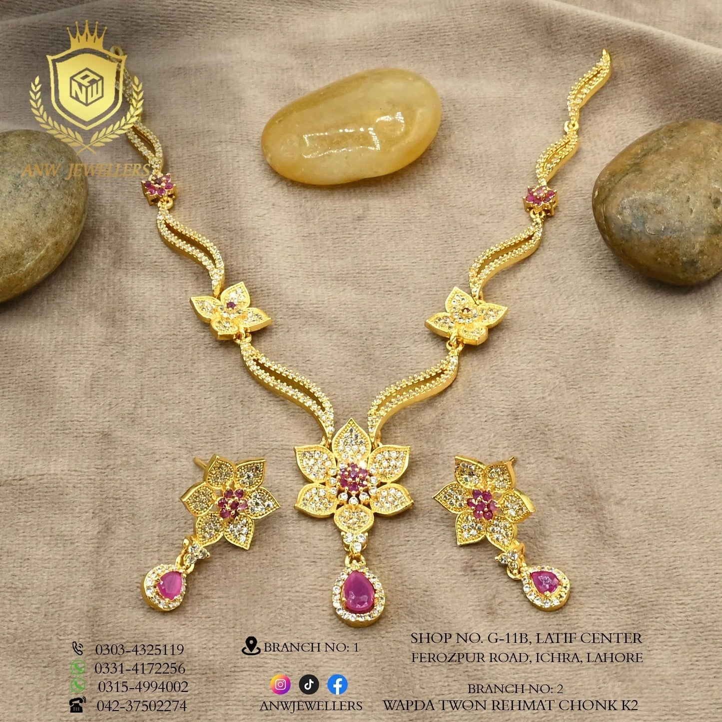 Gold jewelry set with floral ruby and diamond designs on a beige fabric, Anw Jewellers logo visible.