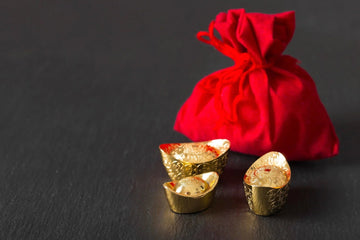 Gold ingots and red pouch on black background, symbolizing wealth and prosperity