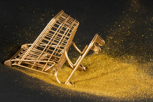 Overturned gold shopping cart in gold glitter on black background, gold price concept