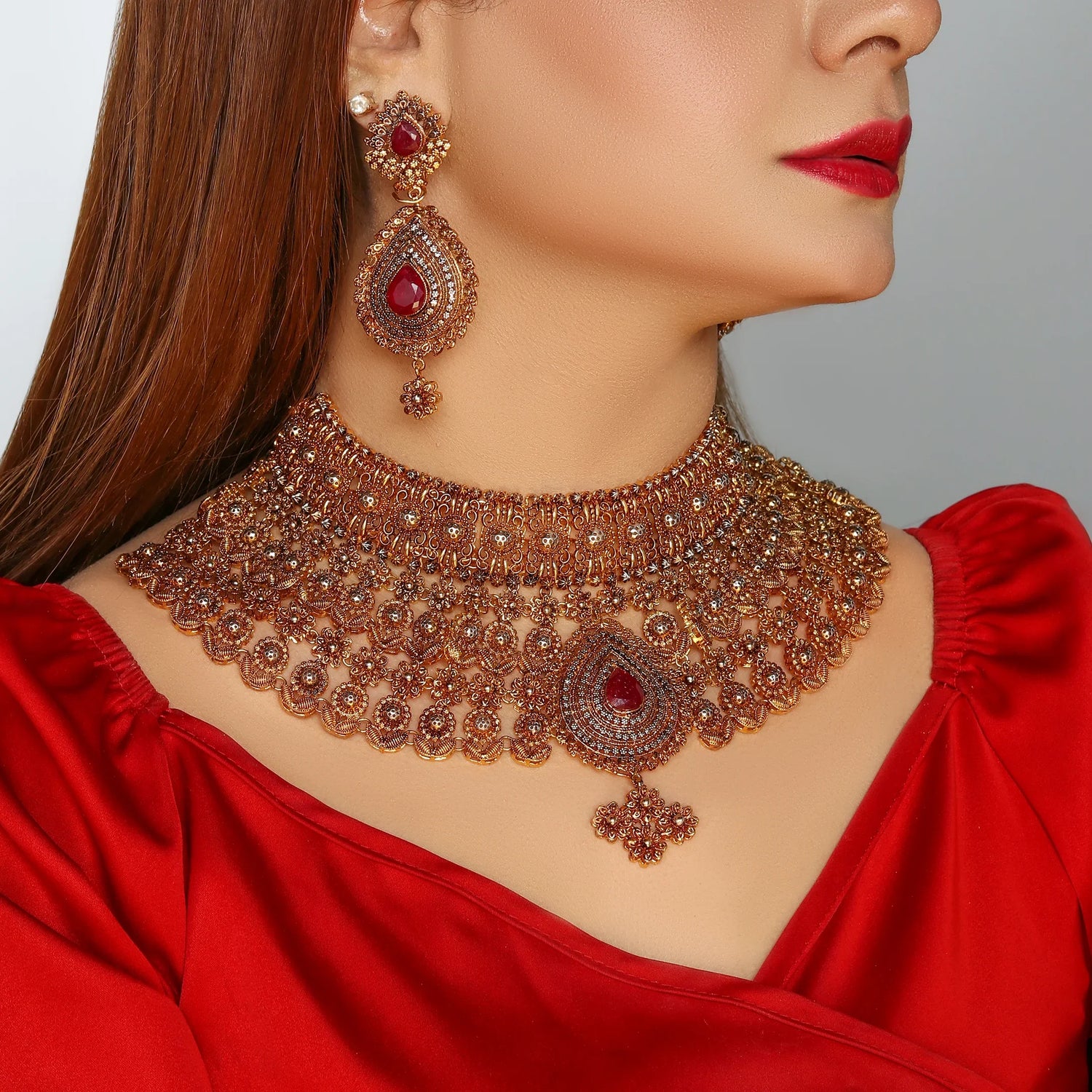 Woman wearing ornate gold and red stone jewelry set with matching necklace and earrings
