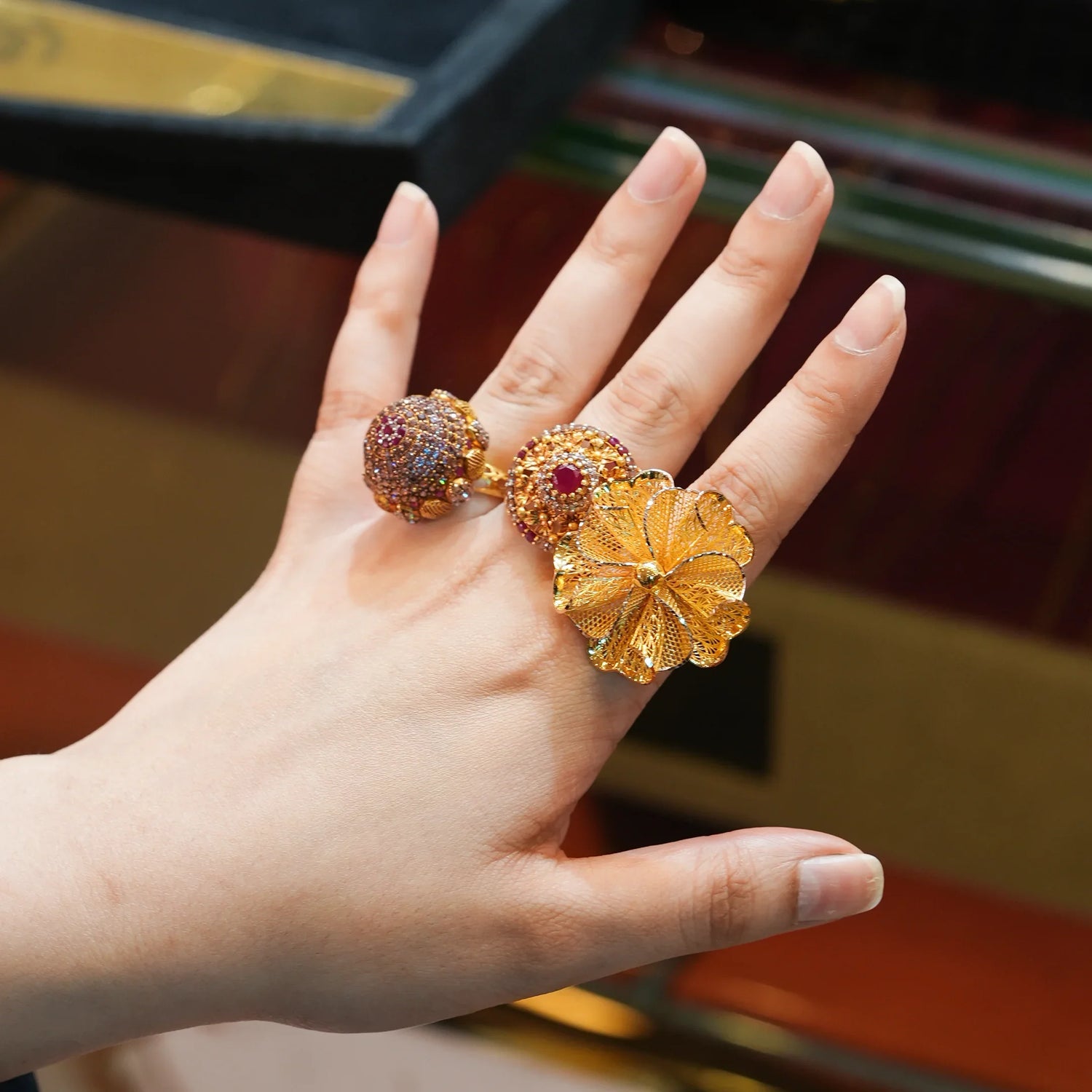 Hand wearing ornate gold fashion rings with floral and gemstone designs